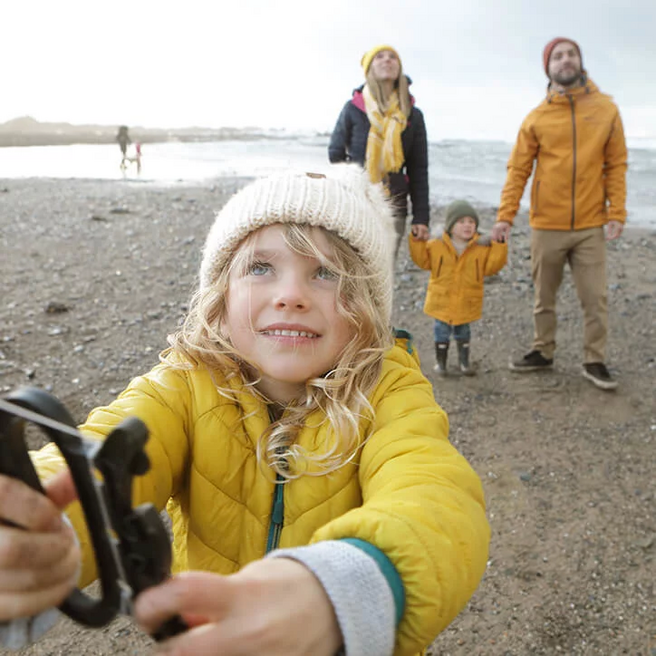 Kind lässt am Strand Drachen steigen, Familie steht im Hintergrund